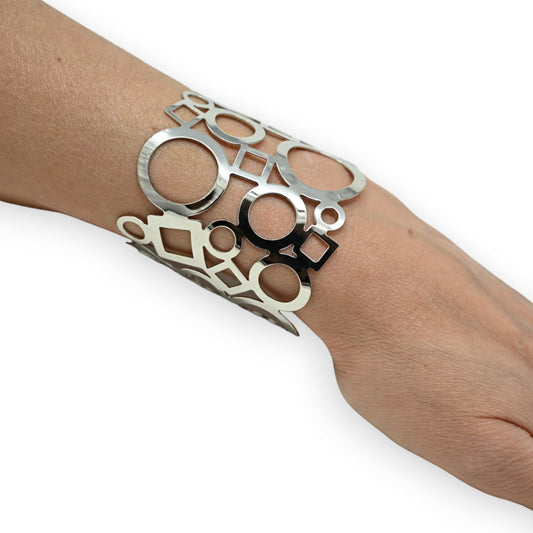 Modernes silbernes Manschettenarmband mit geometrischem Muster aus Kreisen und Quadraten auf einem Handgelenk