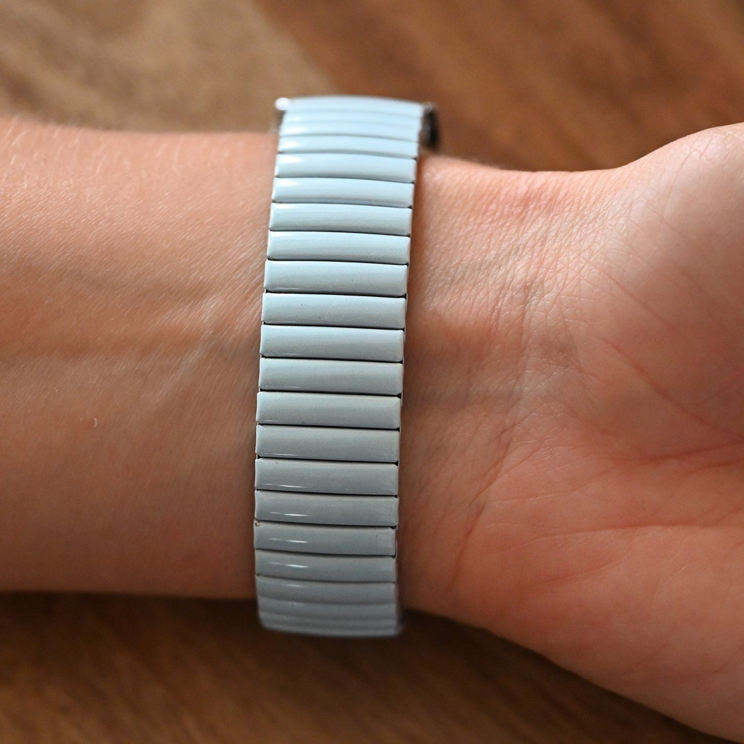 Silbernes Armband mit glatten, länglichen Gliedern auf einem Handgelenk vor einem hölzernen Hintergrund