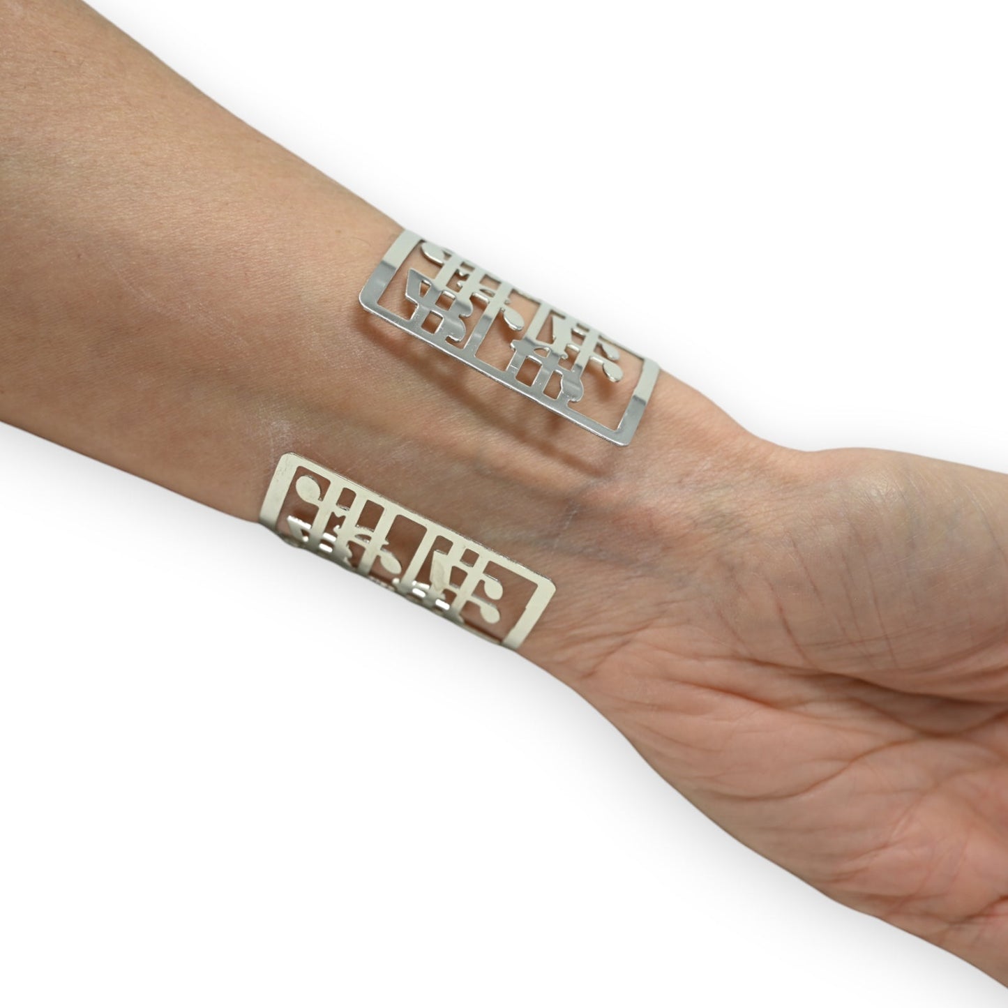 Silberne Manschettenarmbänder mit Musiknoten-Design auf einem Handgelenk, künstlerischer Schmuck für Musikliebhaber