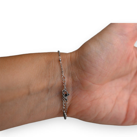 Schlankes silbernes Stahlarmband mit feiner Kette und zwei dekorativen Ringen am Handgelenk einer Person