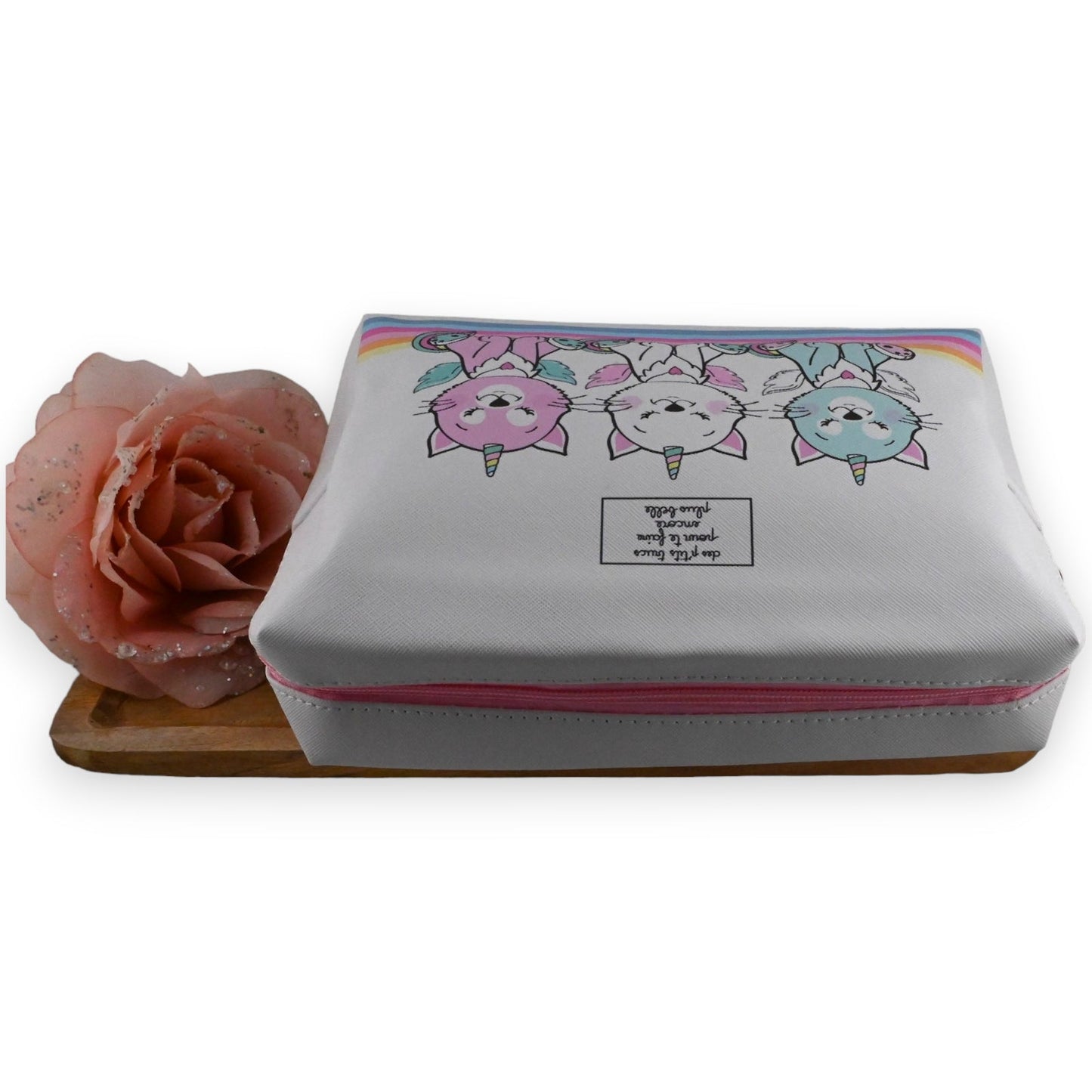 Weiße Toilettentasche mit Einhorn-Katzen-Motiv und Rosa-Blume auf Holzuntergrund, Reise-Kosmetiktasche