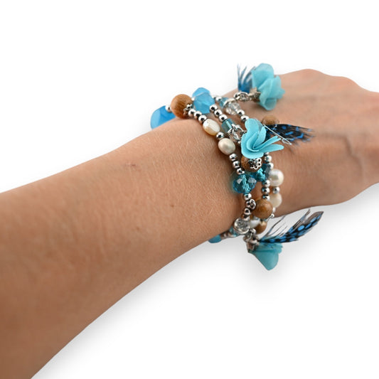 Elastische Modeschmuckarmbänder mit türkisfarbenen Blüten, Federn, Perlen und Kristallen am Handgelenk einer Frau