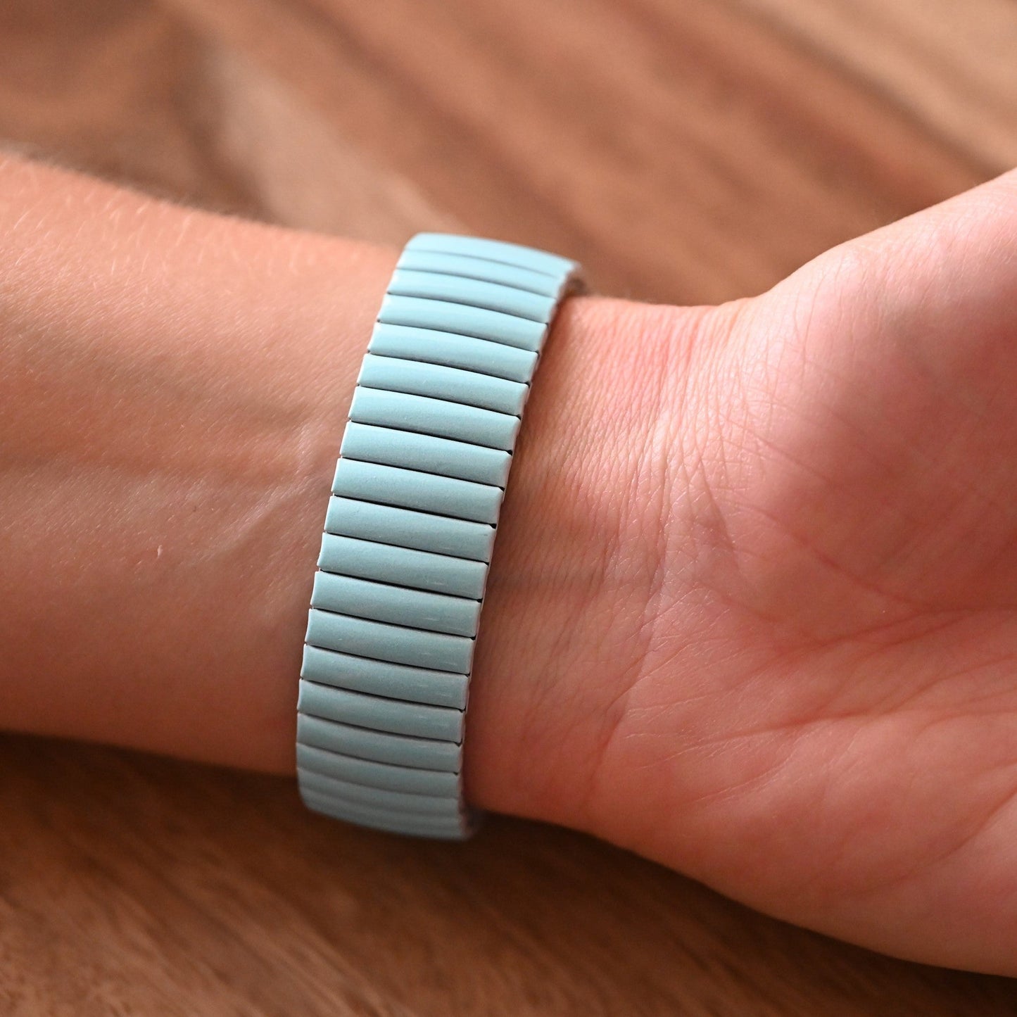 Türkisfarbenes Armband mit elastischen Segmenten am Handgelenk auf Holzuntergrund, Nahaufnahme