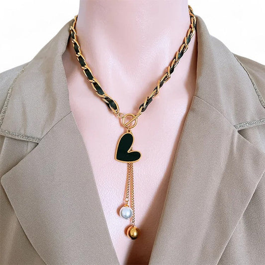 Elegante vergoldete Stahlkette mit schwarzem Herzanhänger, Perlen und goldenen Kugeln auf beigem Blazer