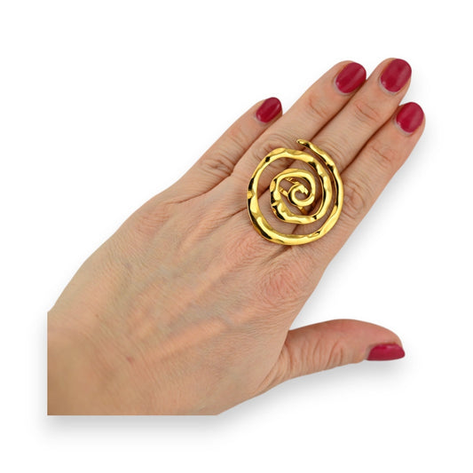 Verstellbarer goldener Spiralring aus Edelstahl an einer Hand mit rot lackierten Nägeln auf weißem Hintergrund