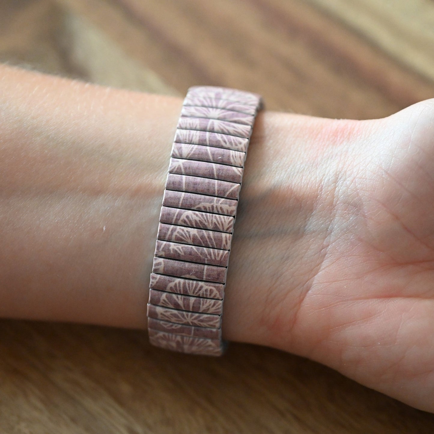 Metallarmband mit geprägtem Blattmuster in Rosa, auf Handgelenk getragen, auf Holzuntergrund