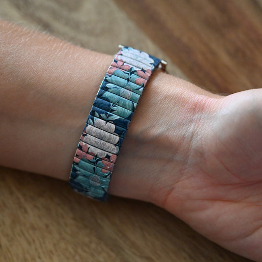 Farbenfroher Vintage-Armreif mit Blumenmuster auf Handgelenk, türkis-rosa Stretcharmband im Retro-Look