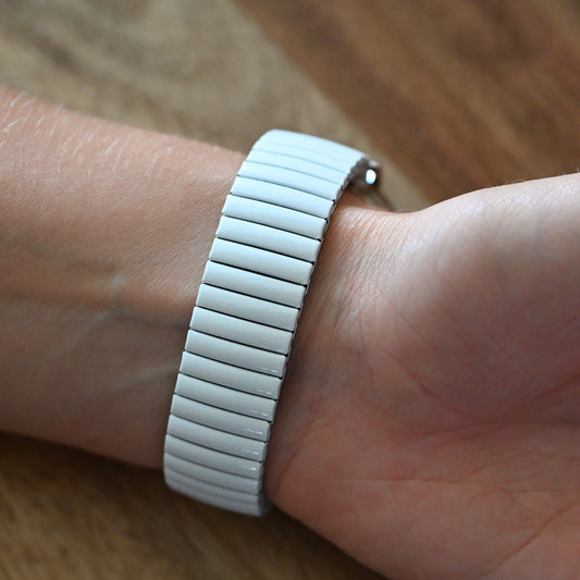 Weißes Metall-Armband einer Uhr am Handgelenk, eng anliegend mit horizontalen Segmenten, auf Holzuntergrund