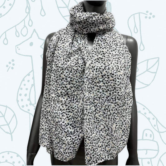 Eleganter Schal mit schwarz-weißem Leopardenmuster auf Schaufensterpuppe, vor einem Hintergrund mit floralen Mustern