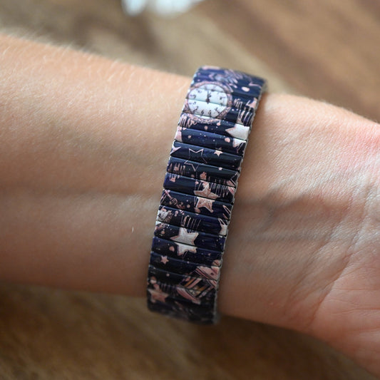 Armband mit nachtblauem Sternenhimmelmuster und kleiner Uhr, getragen am Handgelenk auf Holzuntergrund
