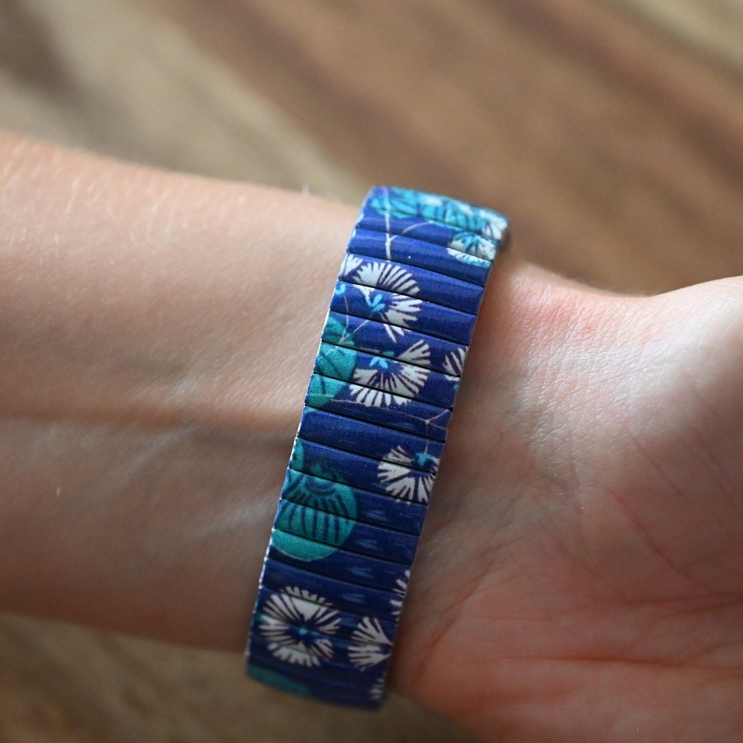 Elastisches Armband mit blau-türkisem Blumenmuster auf Handgelenk, detailreich und farbenfroh