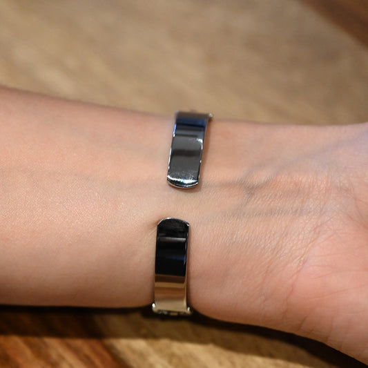 Silberne Armbanduhr mit glattem, metallischem Armband am Handgelenk auf Holzuntergrund, Nahaufnahme