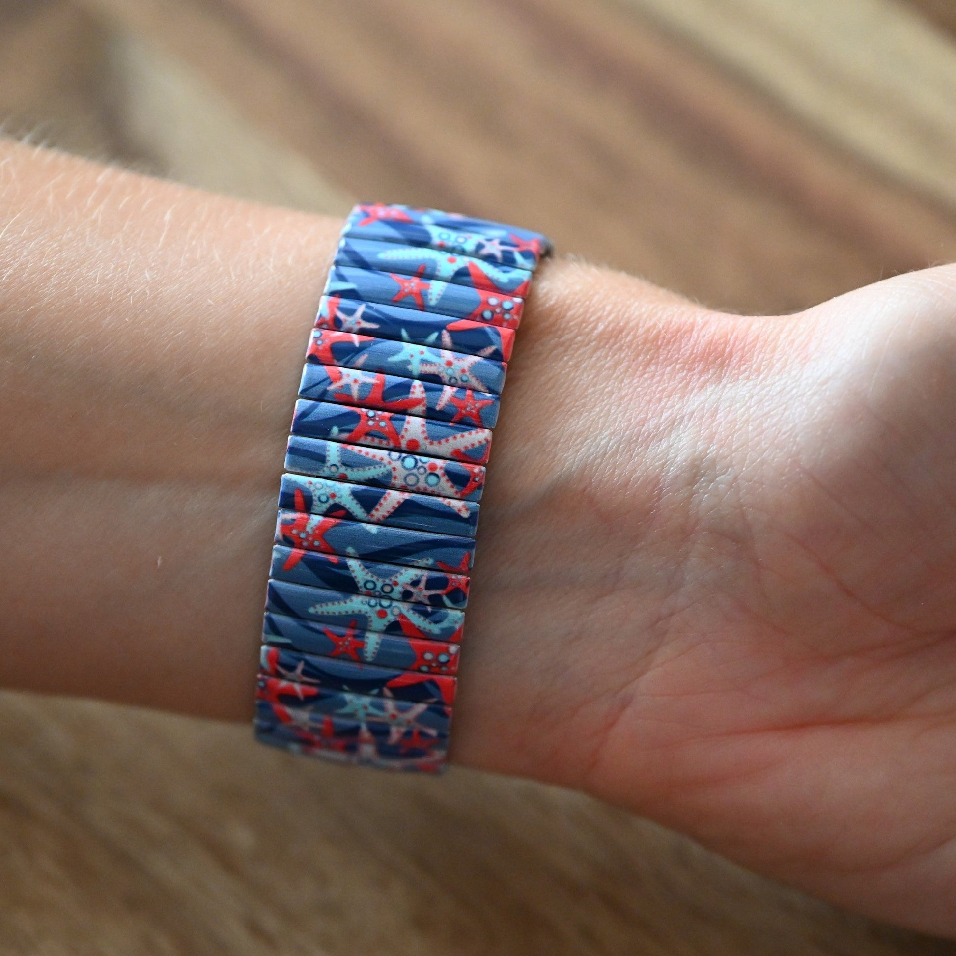 Blaues Stretcharmband mit buntem Seestern-Muster am Handgelenk, auf Holzuntergrund fotografiert