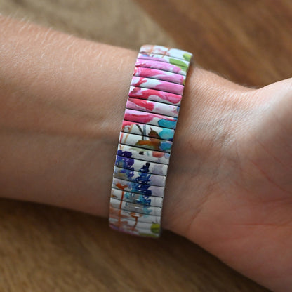 Bunte Armbanduhr mit Blumenmuster auf flexiblem Metallarmband, getragen am Handgelenk auf Holzuntergrund