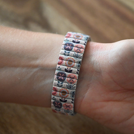 Elastisches Armband mit geometrischem Blumenmuster in Pastellfarben, am Handgelenk getragen, auf Holzuntergrund