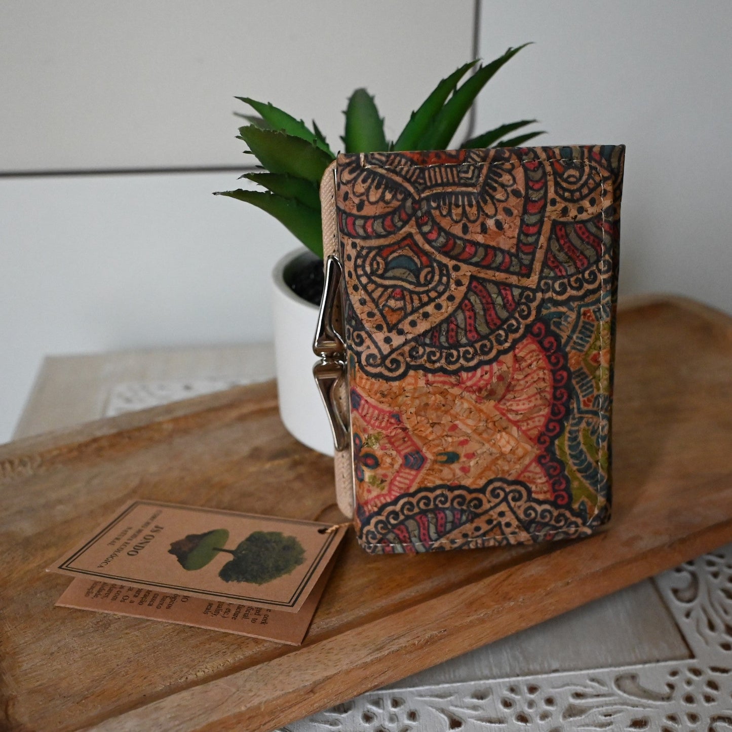 Bunte Kork-Brieftasche mit Mandala-Muster neben Pflanze und Holzkarte auf rustikalem Holztisch, Eco-Lifestyle