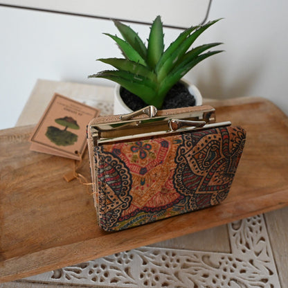 Kompakte Brieftasche aus Kork mit buntem Paisleymuster auf Holztisch neben Sukkulente und Buch, Bohemian-Stil