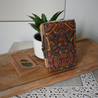 Bunte kompakte Kork-Geldbörse mit orientalischem Muster neben Pflanze und Holztag auf rustikalem Holzbrett