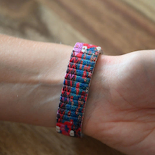 Buntes Armband mit Blumenmuster auf einem Handgelenk, überwiegend in Blau und Rot gehalten
