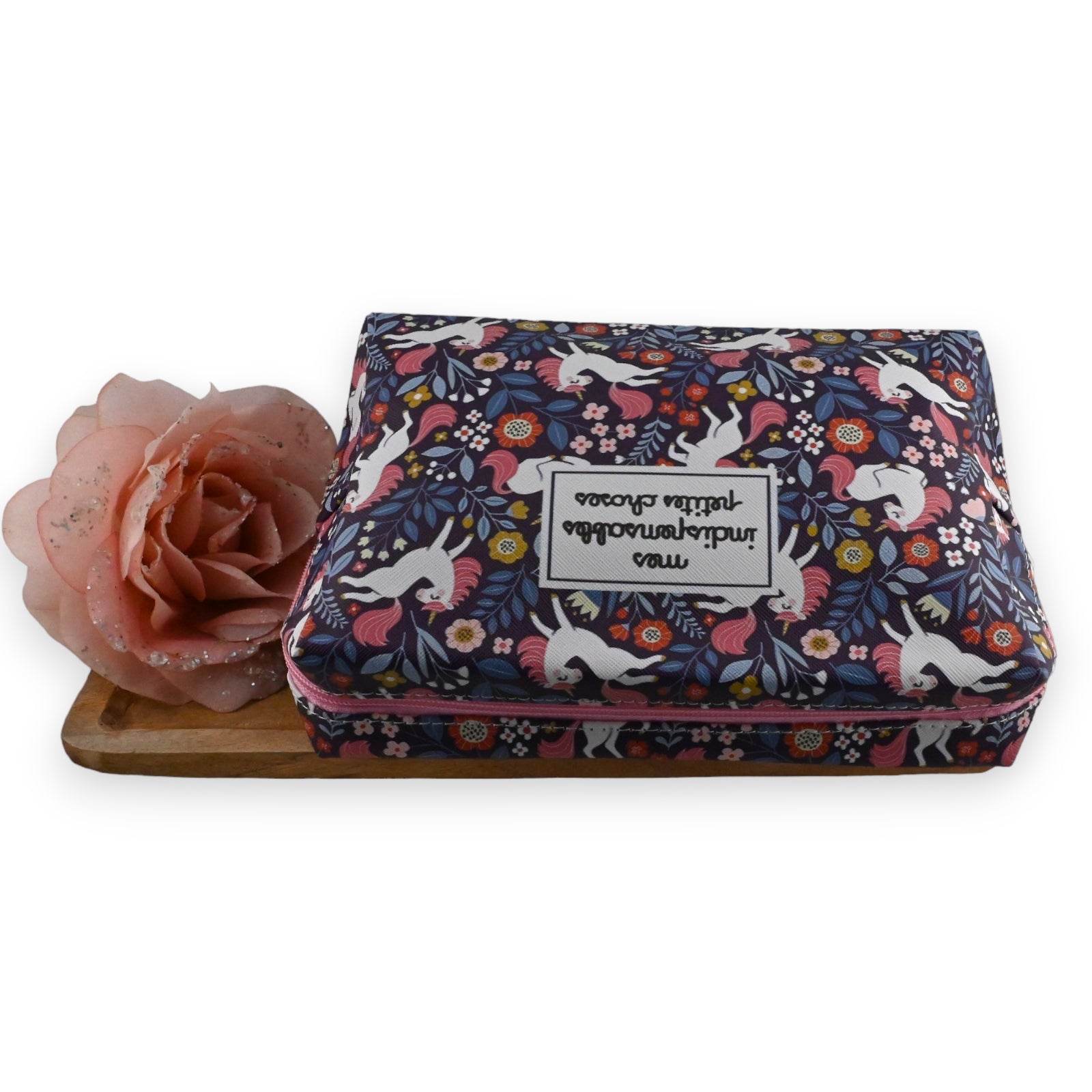 Bunte Kosmetiktasche mit Einhorn-Muster und Blumen, daneben eine rosa Rose auf Holzuntergrund