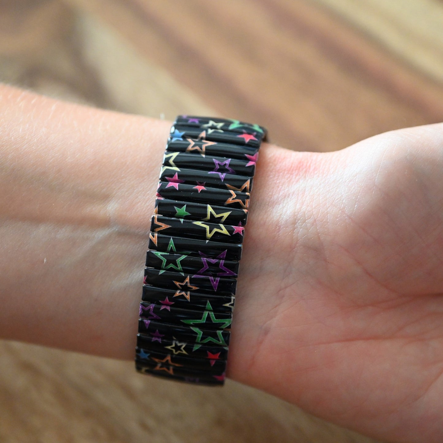 Schwarzes Armband mit bunten Sternen auf Handgelenk, elastisches Design mit farbenfrohem Sternenmuster auf dunklem Grund