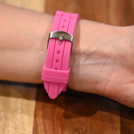 Rosafarbenes Silikonarmband einer Armbanduhr mit silberner Schnalle am Handgelenk einer Person auf Holzuntergrund