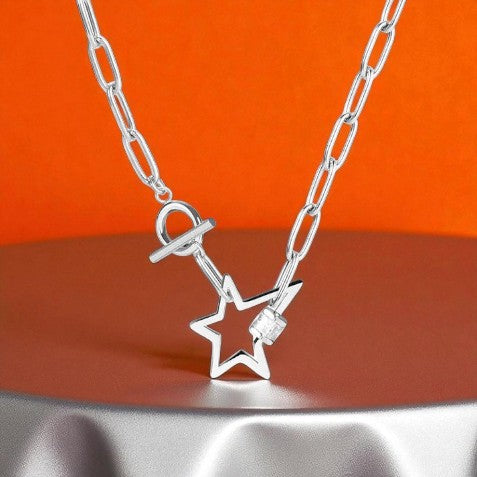 Silberne Halskette mit Sternanhänger und Toggle-Verschluss, vor orangem Hintergrund