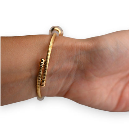 Goldenes Armband mit starrem Design und weißen Akzenten am Handgelenk getragen, eleganter Schmuck für Damen