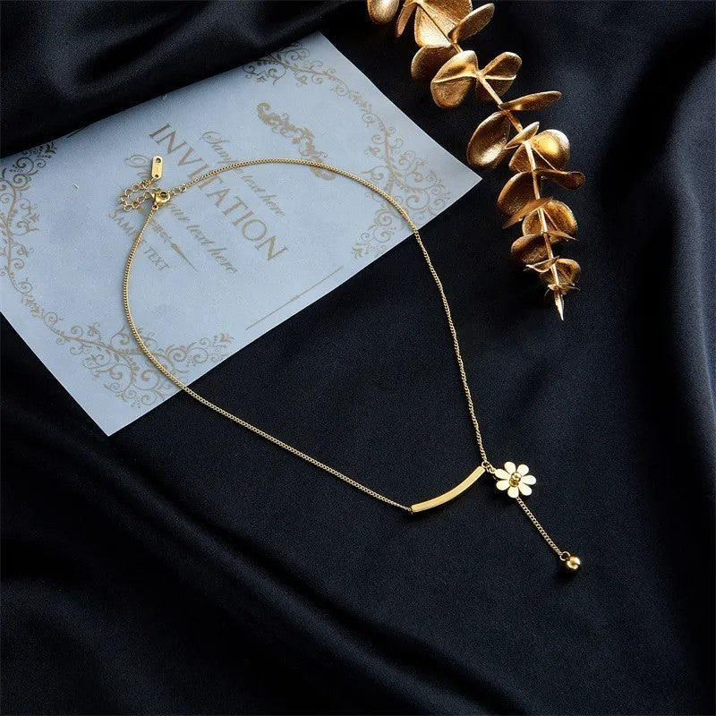 Elegante vergoldete Halskette mit Gänseblümchenanhänger auf schwarzem Hintergrund neben Einladung und goldener Dekoration