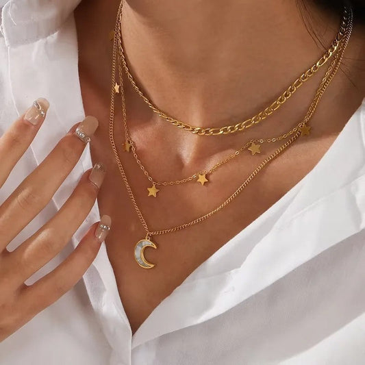 Mehrreihige goldene Halskette mit Stern- und Mondanhängern auf Dekolleté, weiße Bluse und gepflegte Fingernägel