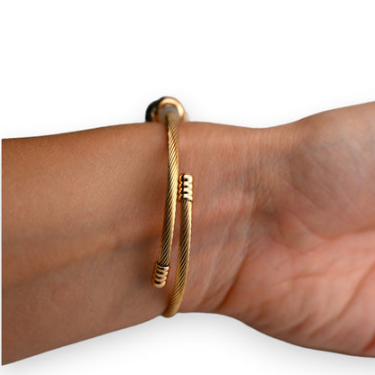 Goldenes Armreif mit gedrehtem Kabeldesign, am Handgelenk getragen. Elegantes Schmuckstück mit feinen Details.