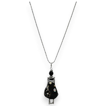 Halskette mit Anhänger: Kleine schwarze Gelenkpuppe im Kleid, verziert mit Blume und Glitzersteinen, an silberner Kette