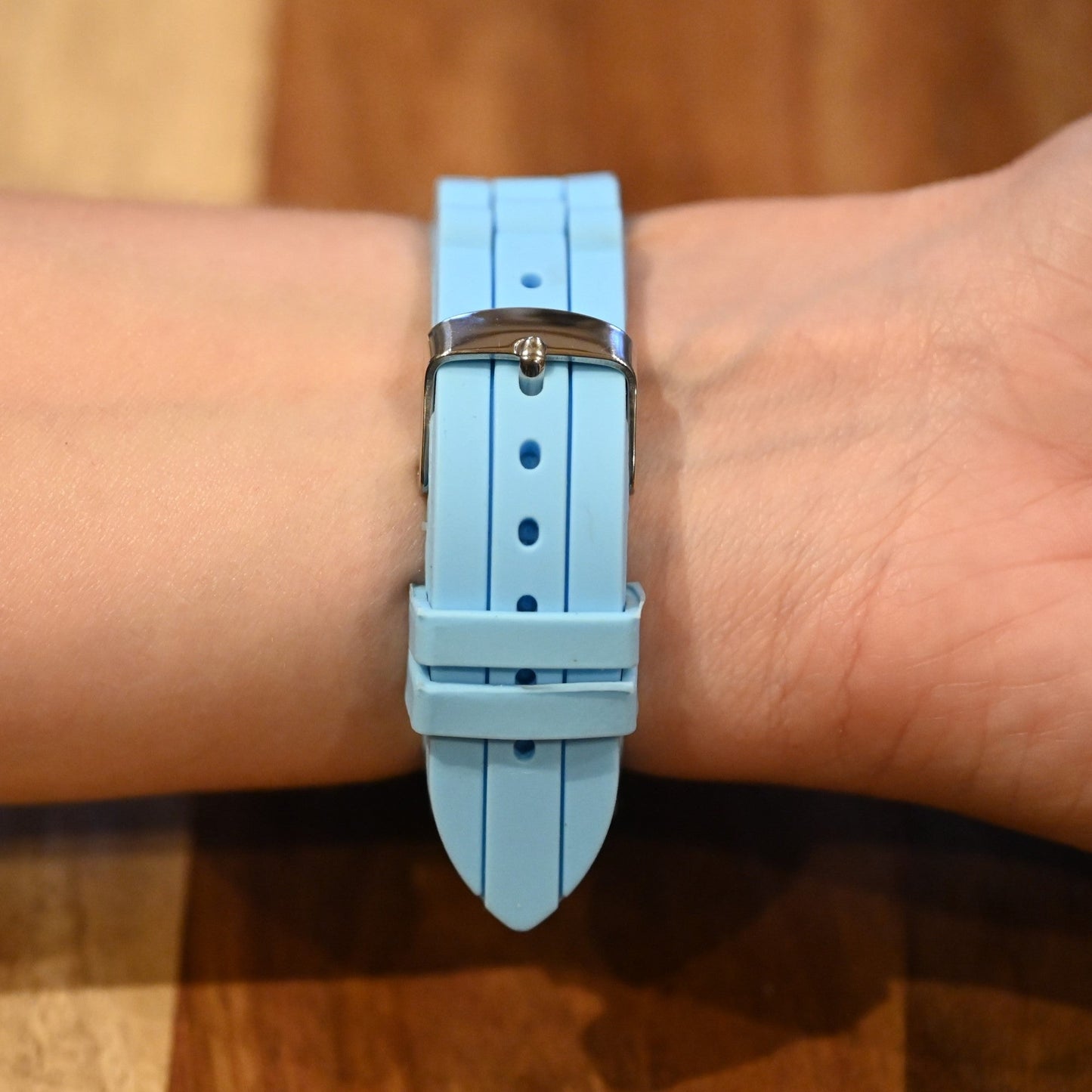 Hellblaues Silikonarmband einer Uhr am Handgelenk, mit silberfarbener Schnalle und gestreiftem Muster