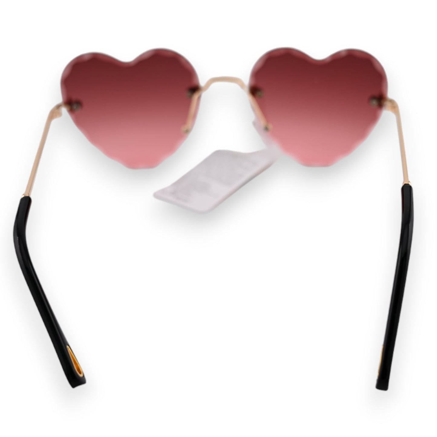 Herzförmige Sonnenbrille mit rosa-braunem Farbverlauf, goldenen Bügeln und schwarzen Enden. Weißer Hintergrund.