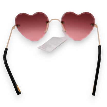 Herzförmige Sonnenbrille mit rosa-braunem Farbverlauf, goldenen Bügeln und schwarzen Enden. Weißer Hintergrund.