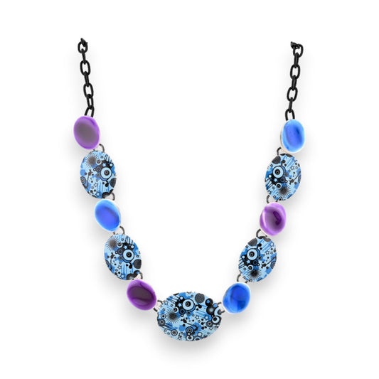 Stilvolle Halskette mit blau-violetten Perlen und ovalen Anhängern mit abstraktem Grafikmuster, an schwarzer Kette