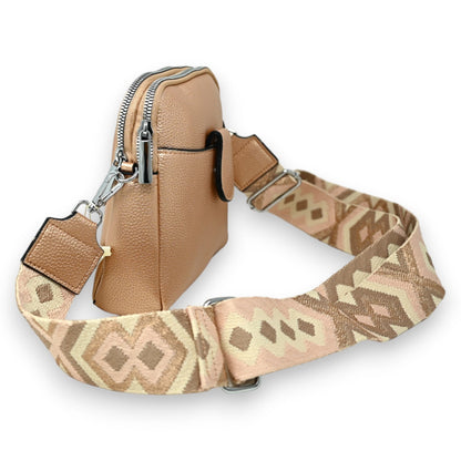 Kompakte metallisch-rosa Umhängetasche mit gemustertem Riemen, Reißverschluss und Lederanhänger, auf weißem Hintergrund