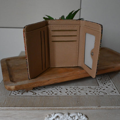 Kompakte Brieftasche aus Kork, geöffnet auf Holzunterlage. Mehrere Kartenfächer und ID-Fenster sichtbar. Neben dekorativer...