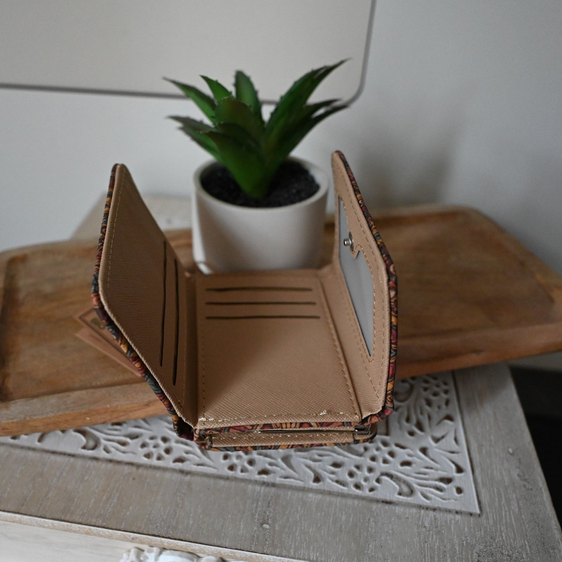 Kleine Kork-Geldbörse geöffnet auf Holztisch mit weißer Spitzendecke und Sukkulente im Hintergrund