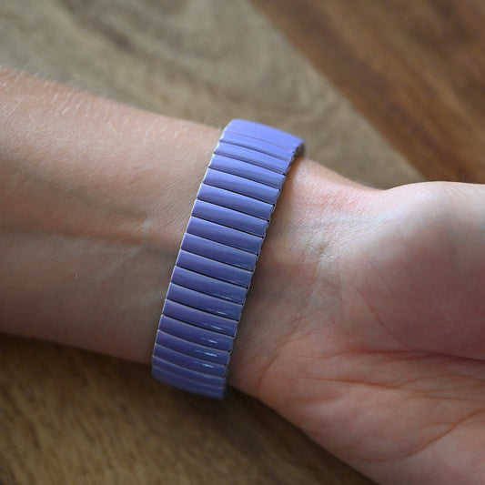 Lilafarbenes Armband mit elastischem Metallband am Handgelenk einer Person auf Holzuntergrund