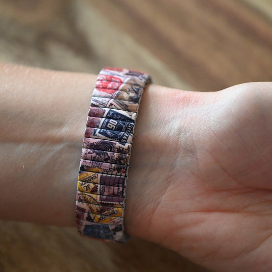 Armband aus Briefmarken-Patchwork in Rot, Blau und Gelb auf einem Handgelenk, kreatives Upcycling-Schmuckstück