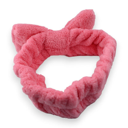Flauschige pinkfarbene Stirnbinde aus weichem Plüschmaterial für Make-up und Gesichtspflege, auf weißem Hintergrund