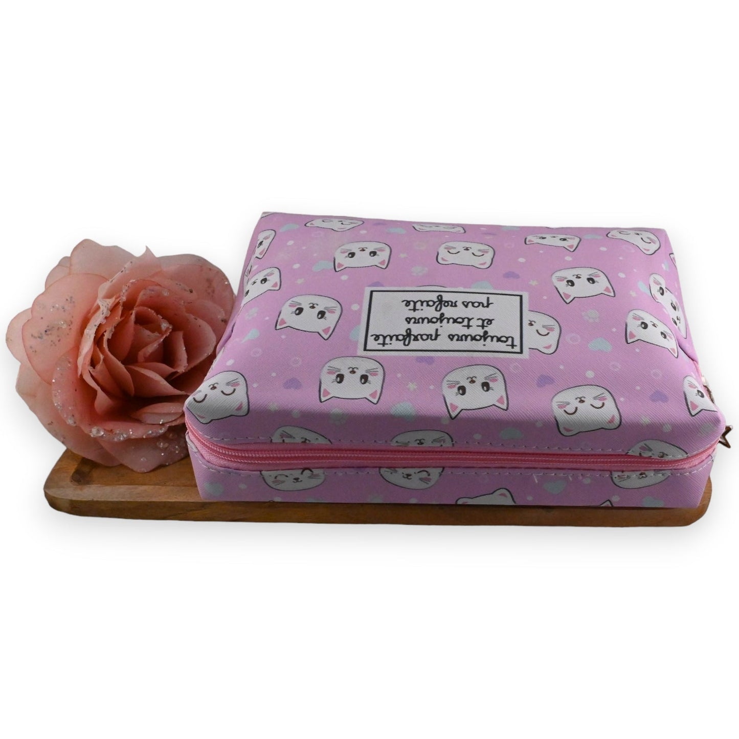 Rosa Kosmetiktasche mit Katzenmotiv, dekorative Rose und Holzbrett. Aufschrift 'Parfume toujours et j'arrive' auf Tasche