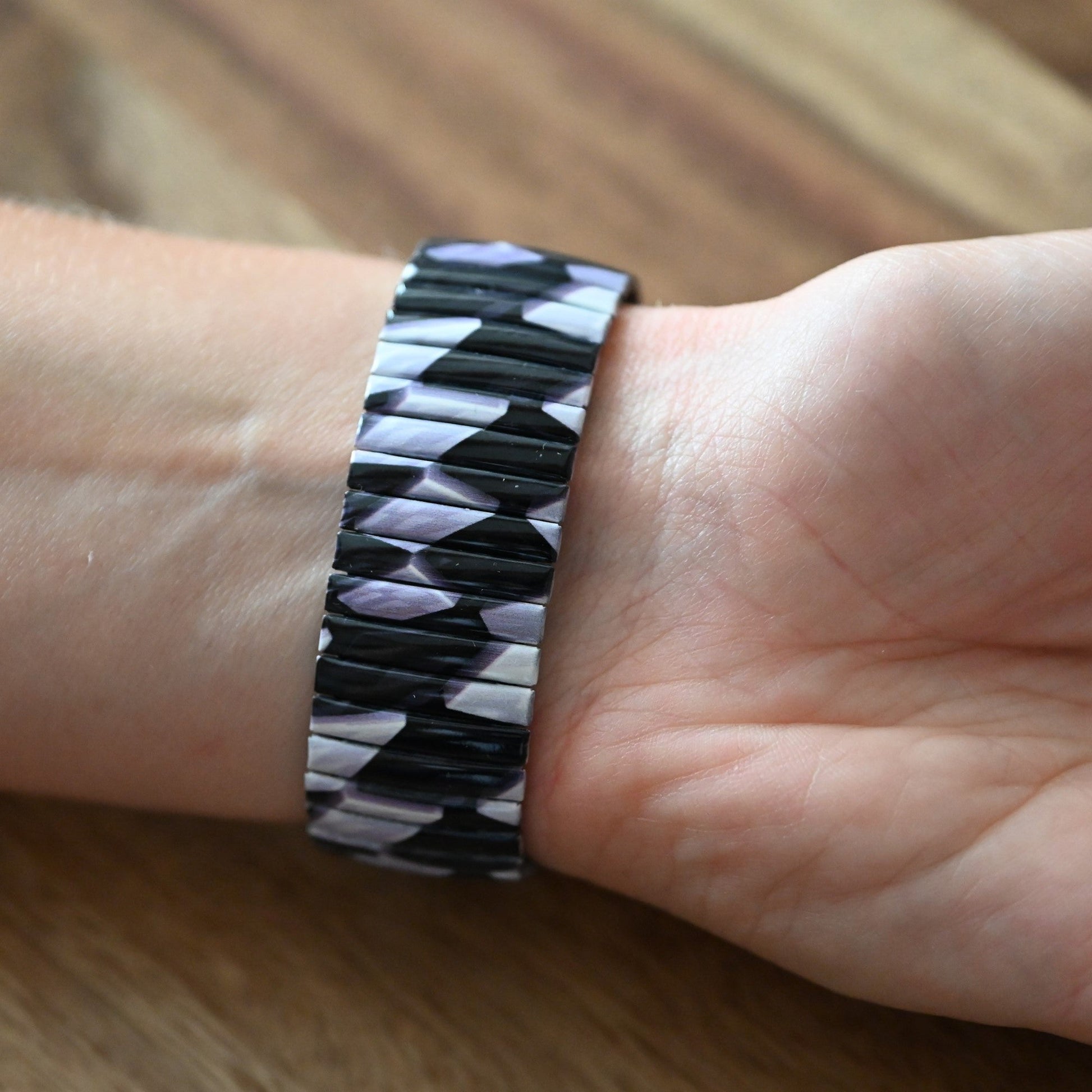 Schwarz-weißes geometrisches Armband mit Zickzack-Muster auf Handgelenk, auf Holzuntergrund