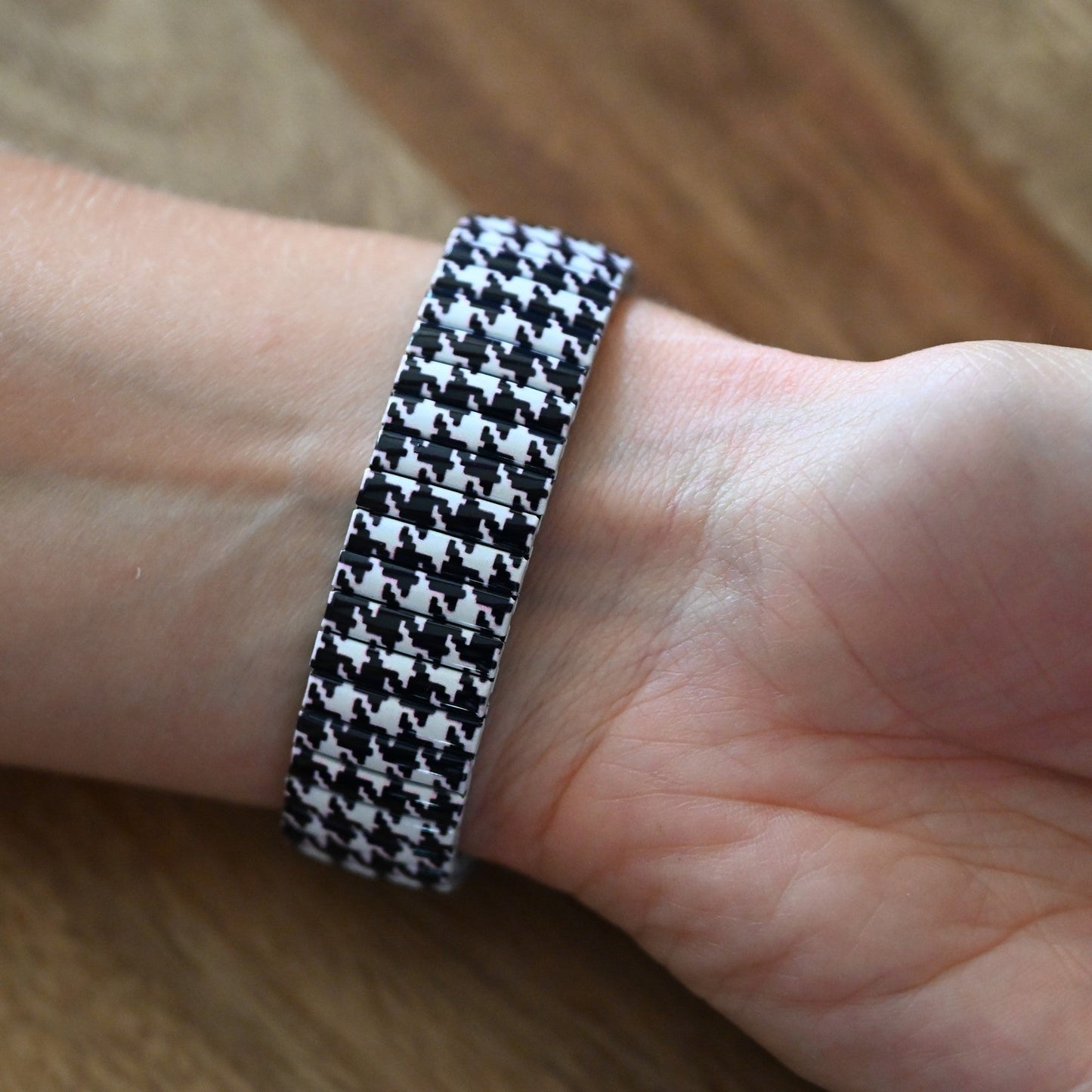 Armband mit schwarz-weißem Hahnentrittmuster am Handgelenk einer Person auf Holzuntergrund