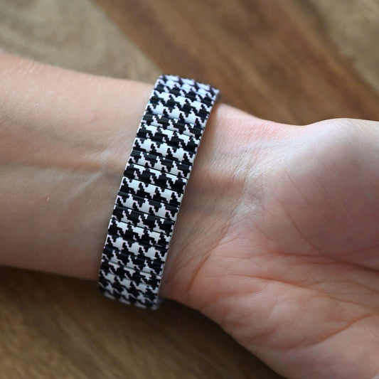 Armband mit schwarz-weißem Hahnentrittmuster am Handgelenk einer Person auf Holzuntergrund