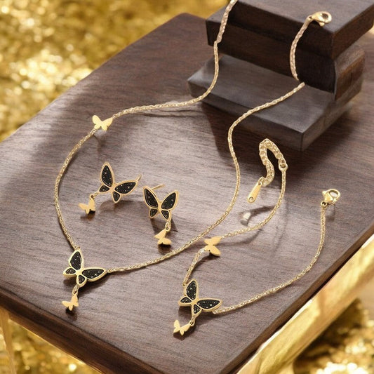 Goldenes Schmuckset mit schwarzen Schmetterlingen und Sternen: Halskette und Ohrringe auf Holzunterlage