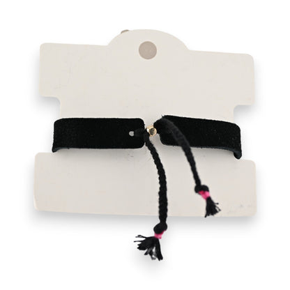 Schwarzes Stoffarmband auf weißem Karton, mit zwei Quasten und pinken Akzenten, modisches Accessoire