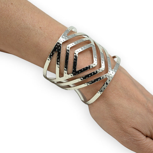 Silberner Armreif mit geometrischem Diamantmuster, getragen am Handgelenk. Moderner, mehrschichtiger Schmuck.