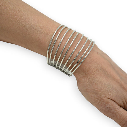 Silbernes Manschettenarmband mit mehreren feinen, durchbrochenen Streifen um ein Handgelenk geschlungen
